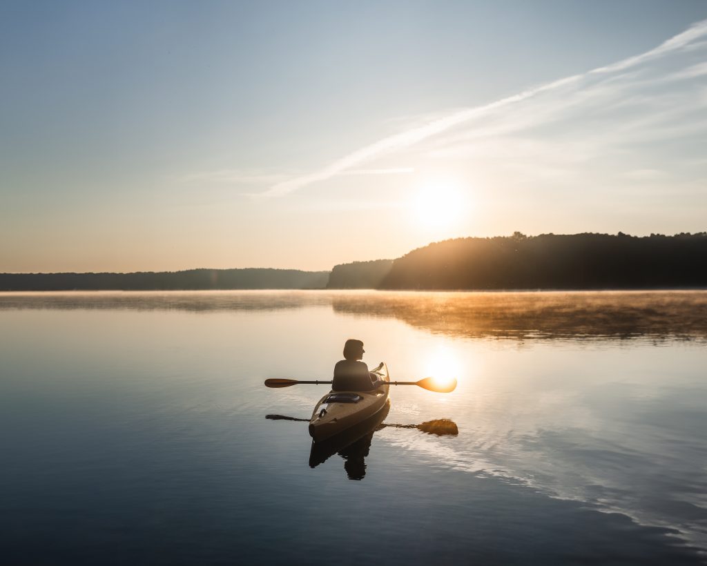 Kanu mit Frau auf einem See an der Mecklenburgischen Seenplatte bei Sonnenuntergang. 