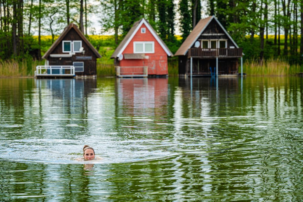 Schwimmerin in einem See in Mecklenburg Vorpommern an der Seenplatte vor Bootshäusern.