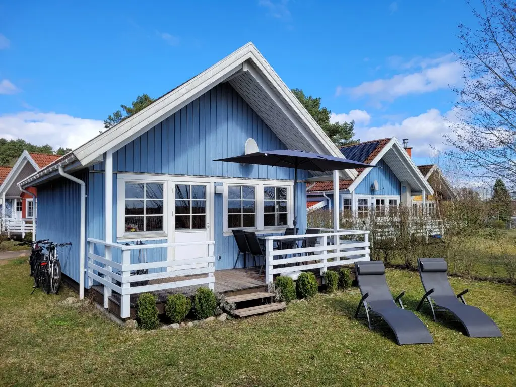 Blaues Ferienhaus Seebrise am Useriner See im skandinavischen Stil aus Holz gebaut mit Terrasse und Sonnenschirm sowie zwei Sonnenliegen für den Urlaub.  